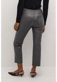 Pantalones cortos de imitación de cuero gris con una cintura elástica, dos bolsillos traseros y una textura suave, combinados con zapatos de tacón negros.