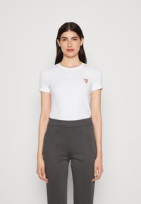 T-shirt bianca a maniche corte con logo a triangolo rosso sul petto, abbinata a pantaloni grigi a vita alta. Tessuto liscio, design semplice.