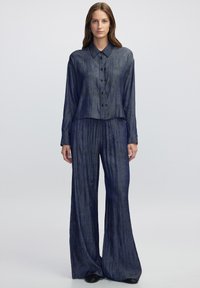 Chemise à manches longues avec col et pantalon large en tissu texturé bleu foncé, présentant des rayures verticales et des fermetures à boutons.