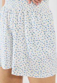 Lightweight shorts feature a gathered waistband, made from soft fabric with a white background and a scattered blue floral pattern.