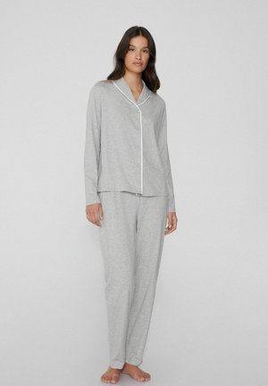 Ensemble de pyjama gris clair en tissu doux, comprenant un haut avec boutons et col, bordé de piping blanc, accompagné de pantalons à taille élastique.