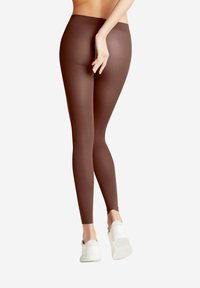 Leggings marron en matériau extensible, coupe ajustée, taille haute, associées à des chaussures de sport blanches, avec une texture lisse et sans motifs visibles.