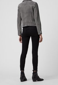 Šedá sukně motocyklová bunda s přiléhavým střihem, zipovými manžetami a klasickým límcem, v kombinaci s černými skinny džíny a kotníkovými botami.