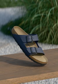 Sandales bleu marine avec deux boucles ajustables, semelle en liège et semelle en caoutchouc texturé, posées sur une surface en bois.