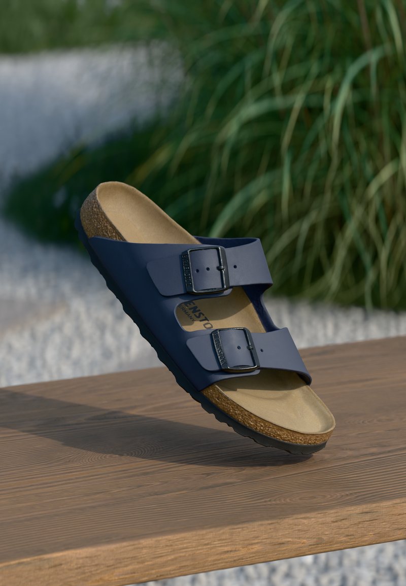 Sandales bleu marine avec deux boucles ajustables, semelle en liège et semelle en caoutchouc texturé, posées sur une surface en bois.