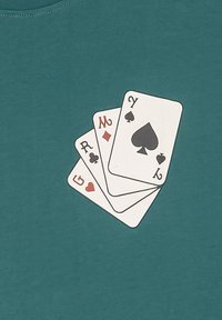 Camiseta turquesa con un gráfico de cuatro cartas de juego: dos diamantes rojos, un corazón rojo y una pica negra, impresas en el frente.