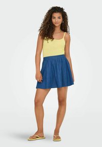 Canotta gialla in maglia abbinata a una gonna di jeans blu. L'outfit presenta una vita aderente e un orlo svasato, completato da semplici sandali.