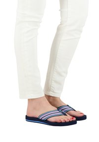 Infradito blu con fasce in tessuto a strisce multicolori. Suole morbide e imbottite, con un accento blu lungo il bordo, indossate con pantaloni bianchi.