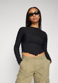 Svart cropped langermet topp med teksturert stoff og bølgete kant. Kombinert med lyse khaki cargo-bukser, som har sidelommer og knappefeste.