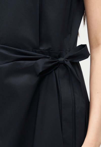 Robe noire avec une ceinture en tissu nouée autour de la taille, montrant le côté d'un bras nu.