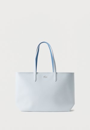 Vaaleansininen, teksturoidulla pinnalla varustettu olkalaukku, jossa on kaksi kahvaa ja pieni hopeinen krokotiililogolla varustettu etukeskiosa valkoista taustaa vasten.