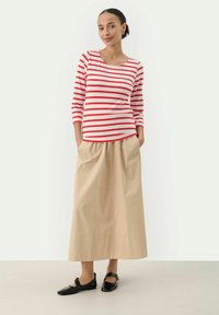 Stribet rød og hvid langærmet bluse parret med en beige, løstsiddende, ankellang nederdel. Sorte flade sko fuldender outfittet.