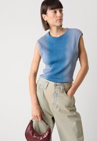 Haut sans manches bleu à rayures, texture douce, associé à un jean baggy délavé. Tiens un sac à main en vernis bordeaux avec un design incurvé.