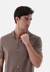 Polo shirt marrone a maniche corte con chiusura a bottoni, caratterizzato da una morbida texture e un design classico del colletto.