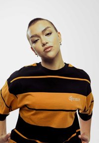 Zwarte en oranje gestreepte oversized t-shirt met korte mouwen en een zachte textuur. Bevat het woord "Grimey" in witte schrift op de borst.