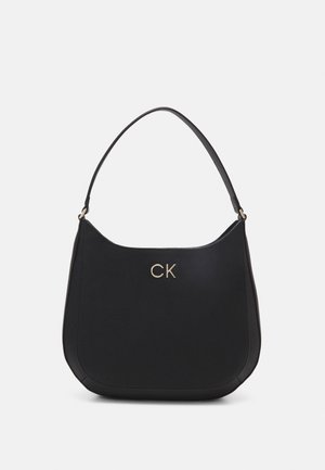 Sort skuldertaske i læder med en enkelt rem og et gyldent "CK"-logo centreret på forsiden mod en ensfarvet baggrund.