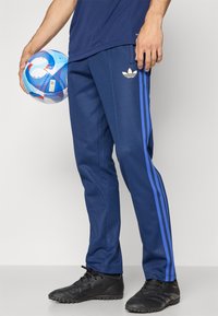 Calças de atletismo da marinha com riscas azuis, feitas de tecido suave. Com um logótipo bordado e um design ajustado, combinadas com sapatilhas desportivas pretas.