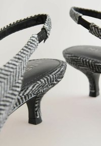 Čierno-biely houndstooth vzor na textilnom povrchu, otvorená špička a úzky podpätok. Čierne kožené stielky s viditeľným logom značky.