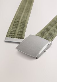 Cintura verde intrecciata con superficie testurizzata e fibbia rettangolare in metallo argentato. Le estremità sono rifinite con dettagli metallici lisci.