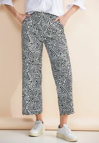 Pantalons noirs et blancs à motif géométrique en triangles, avec poches et longueur cropped, associés à des baskets blanches.