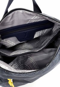 Interior de bolso de mano con patrón en azul marino y blanco, con forro gris, que cuenta con un bolsillo con cremallera, múltiples compartimentos y detalles textuales.