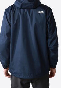 Chaqueta impermeable azul marino con capucha ajustable, puños elásticos y detalle de logo blanco en la parte trasera. Tejido liso y ligero.