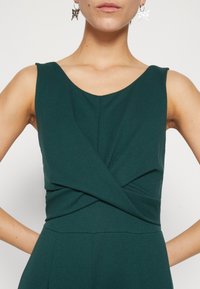 Robe sans manches verte avec un décolleté en V et un design croisé à la taille. Fabriquée à partir d'un tissu texturé avec des détails de couture remarquables.
