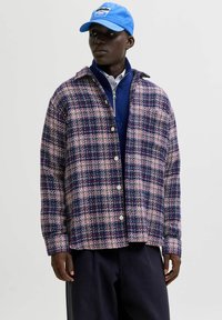 Tamsiai mėlynas ir rožinis languotas marškiniai su sagomis, pagaminti iš tekstūruoto audinio, su apykakle ir laisvu siluetu. Dėvimi ant mėlynos užtrauktuko striukės.