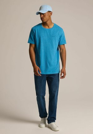 Niebieska t-shirt o fakturze, krótkie rękawy, okrągły dekolt, w połączeniu z ciemnoniebieskimi dżinsami i białymi sneakersami. Jasnoniebieska czapka z detalem logo.