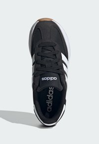 Čierna atletická obuv s bielymi pruhmi, s textilným vrchom, okrúhlou špičkou, šnurovacím dizajnom a gumovou podrážkou s hnedým akcentom.