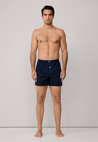 Marineblauwe zwembroek met verticale strepen, voorzien van een elastische tailleband, een enkele knoop aan de voorkant en een comfortabele pasvorm.