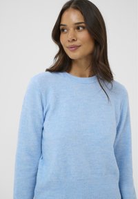 Svetlo modra puli iz mehkega materiala z okroglo vratu in rebrastim robom. Tekstura je gladka z rahlo variationo v barvi.