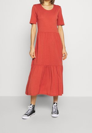 Femme portant une robe rouge courte aux manches courtes, longueur mollet, associée à des baskets montantes noir et blanc, debout devant un fond uni.