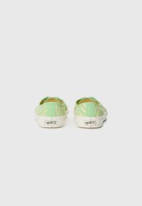 Green slip-on shoes with a light tan zebra stripe pattern, white rubber soles, and a textured canvas upper. Visible brand logo on the heel.