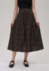 Svart midi kjol med ett leopardmönster i bruna toner, veckad midja och vid, flödande silhuett. Kombinerad med platta svarta skor.