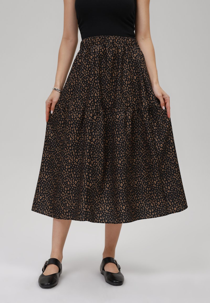 Svart midi kjol med ett leopardmönster i bruna toner, veckad midja och vid, flödande silhuett. Kombinerad med platta svarta skor.