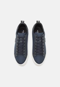Navy blue sneakers with a mesh and synthetic upper, featuring flat laces, a white rubber sole, and a black logo accent on the side.