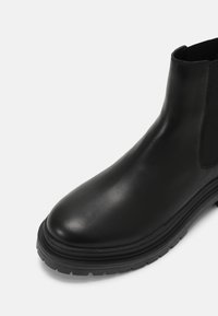 Botín negro de cuero con laterales elásticos, punta redonda, suela texturizada y acabado suave. Presenta un tacón resistente y ligeramente elevado.