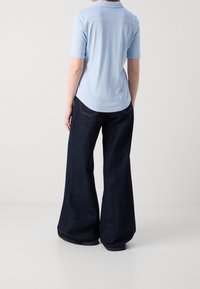 Polo shirt azzurro chiaro a maniche corte, tessuto liscio, orlo curvo. Abbinato a jeans svasati blu scuro, tasche posteriori visibili e cuciture a contrasto.