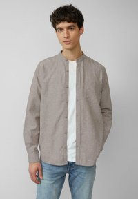 Hellbraunes, langärmliges Hemd mit Knopfleiste und Stehkragen. Über einem weißen Hemd getragen, mit einer Brusttasche und lockerer Passform.