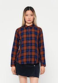 Plaid shirt in brown, blue, and orange tones, featuring a collar, button closure, and long sleeves. Textured fabric with a relaxed fit.