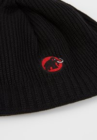 Black knitted beanie with ribbed texture and a red circular patch featuring a black elephant logo with white tusks.
