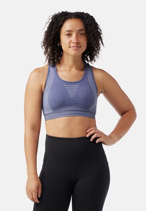 Blue sports bra with a fitted design, featuring a textured fabric, wide straps, and horizontal stitch detail across the front. Paired with black leggings.