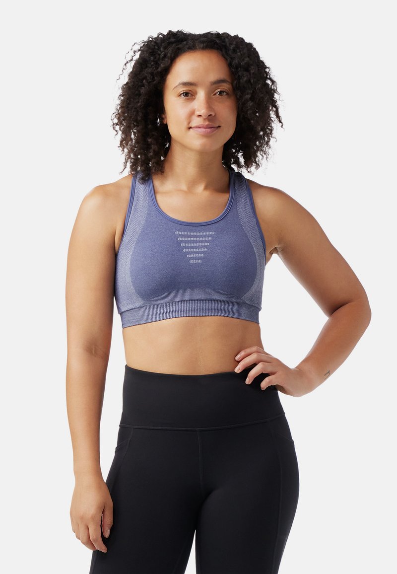 Sininen urheilBra, jossa on tiukka muotoilu, teksturoitu kangas, leveät hihnat ja vaakasaumat etuosassa. Yhdistetty mustiin legginsseihin.