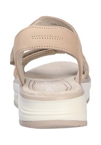 Sandal beige con dos correas ajustables, una plantilla acolchada y una suela texturizada. El tacón es ligeramente elevado con una suela neutra.