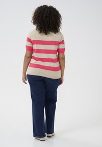 Beige en roze gestreepte trui met korte mouwen, gecombineerd met donkerblauwe jeans en lichtgekleurde schoenen, gezien vanuit de achterkant.