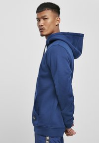 Tengerészkék pamut keverék kapucnis pulóver, elülső kenguruzsebbekkel, állítható húzózsinórral a kapucniban, valamint bordás mandzsettákkal és aljjal.