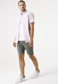 Lichtroze kortom hemshirt met knopen, over een roze t-shirt. Groene opgerolde shorts en witte sneakers met groene accenten.