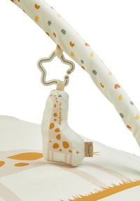 Soft plush giraffe toy with yellow spots, attached to a beige star-shaped teether. Background features a patterned mat with earthy tones.