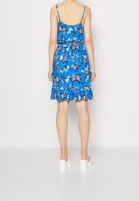 Kukallinen auringonpaiste dressi kirkkaan sinisessä värissä, jossa on säädettävät spagettiolkaimet ja röyhelöhelma. Yhdistetty suurine valkoisiin platform-korkokenkiin.